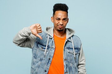 Wall Mural - Young sad man of African American ethnicity wearing denim jacket orange t-shirt showing thumb down dislike gesture isolated on plain pastel light blue background studio portrait. Lifestyle concept.