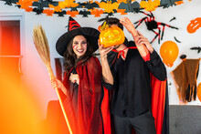 Couple Having Fun Holding Pumpkins And Wearing Dressed Carnival Halloween Costumes And Makeup Posing With Bats And Balloons On Background At The Halloween Party.Halloween Holiday Celebration Concept