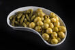 kidney-shaped tray with pickles and olives, placed on a black background