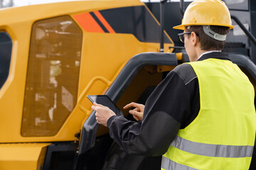 Aufkleber - Worker in a helmet with a digital tablet on the background of construction machine