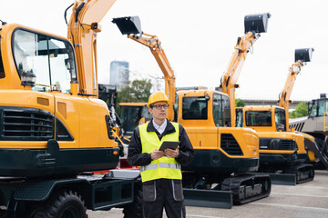 Aufkleber - Engineer in a helmet with a digital tablet stands next to construction excavators.