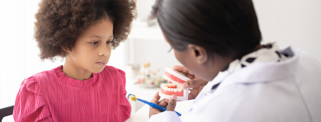 African American dentist explaining to mixed-race afro child how to brush teeth. The doctor and healthcare concept for children.