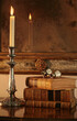 Antique leather-bound books next to a silver candelabra. In the background is an antique Venetian mirror with antique opera glasses resting on books. Stock Image.