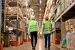 © alfa27 - Back view on unrecognizable Manager and staff talking, discussing while walking in warehouse. caucasian people in factory with safety helmet, vest. industry, job, meeting, work training and teamwork.