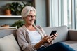 © VERTEX SPACE - casual relax retired old senior woman using smartphone on sofa at home surfting social media peaceful enjoy technology at home