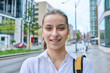 Headshot portrait of teenage girl looking at camera outdoors on city street