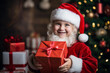 © Evgeniia - Happy little boy dressed as Santa holding a Christmas present in his hands