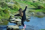 Fototapeta  - Young girl hopping across a stream on stepping stones. 