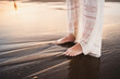 feet of beautiful woman in beautiful white dress on the shore of the beach wet by the waves