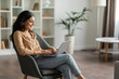 © Home-stock - Freelance concept. Happy hindu lady using computer working online, sitting in comfortable chair at cozy home interior, free space. Internet technology, distance work