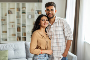 portrait of young romantic indian couple embracing and smiling, posing in living room interior, enjo