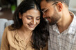 © Home-stock - Tender indian couple embracing, enjoying moment together, sitting on sofa at home, loving spouses bonding. Romantic relationship and affection