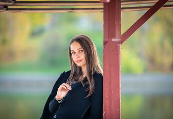 Wall Mural - A beautiful girl poses while standing by a pond under an umbrella in an autumn park.