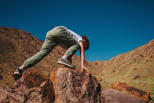 Boy Climbing On Big Boulder In The Mountains