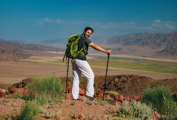 Canvas Print - Hiker on the top of mountain with backpack and trekking poles turned backwards