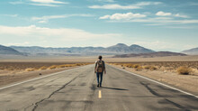 A Person Walking Along An Empty Road In A Desolate Landscape With Blue Sky