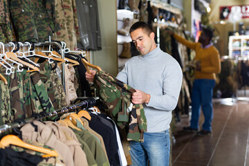 Sticker - European man choosing camouflage clothes in military store. African-american man shopping in background.