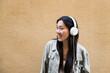 © Cavan - Young happy woman listening music with headphones standing outside.