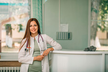 Smiling female doctor with stethoscope standing near reception desk at medical clinic