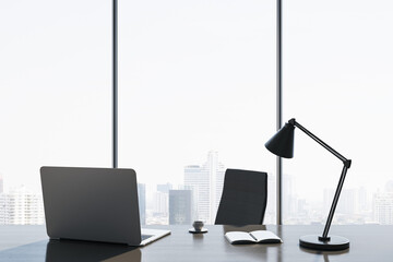 Wall Mural - Close up of modern backlit workplace with laptop, table lamp, coffee cup and panoramic window with city view in the background. 3D Rendering.