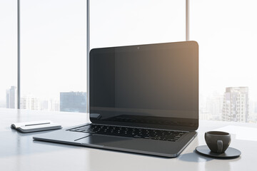 Close up of contemporary workplace with empty mock up laptop screen, supplies, coffee cup and panoramic window with city view in the background. 3D Rendering.