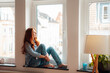 © Westend61 - Thoughtful redhead woman sitting on window sill