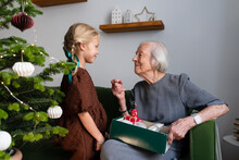 Smiling Girl With Grandmother Holding Box Of Christmas Ornaments At Home