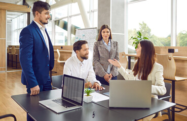 Wall Mural - Team of four business people having corporate staff work meeting. Group of friendly young men and women using modern laptops and having discussion at wooden table in cozy office interior