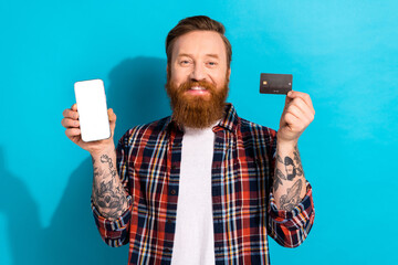 Poster - Photo of handsome man dressed checkered shirt hold credit card presenting smartphone screen empty space isolated on blue color background