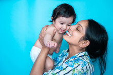 Smiling Indian Mother Playing With Her Six Months Cute Little Baby In Diaper Isolated Over Blue Background. Happy Family. Asian Mom With Infant Child Having Fun, Motherhood. Copy Space.