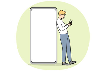 Wall Mural - Young man standing near huge smartphone with mockup screen. Guy pose near cellphone with empty blank copy space display. Vector illustration.