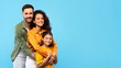 © Prostock-studio - Loving happy european family of three embracing and smiling at camera over blue studio background, panorama, free space