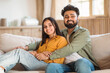 © Prostock-studio - Happy indian lovers enjoying time together at home, sitting on couch, embracing and smiling at camera, free space