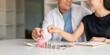© Natee Meepian - Family savings. Happy couple asian putting coin in piggybank while sitting together on desk at home, loving spouse planning budget and saving money for future