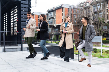 Group of business people walking outside in front of office building. Colleagues discussing on the way to the work. Young employees talking about staff meeting.