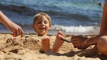 Canvas Print - Child, tickling sibling on the beach on the feet with feather, kid cover in sand, smiling, laughing, enjoying some fun