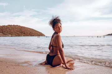 Wall Mural - Beautiful African american woman in pink bikini on tropical beach. Portrait of dark skinned woman smiling at sea. Brunette tanned girl in swimwear enjoying and walking on beach.