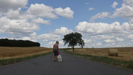 Wall Mural - Beautiful blond child, boy, lying on a haystack in the field. Amazing landscape, rural scene with clouds, tree and empty road summertime, fields of haystack next to the road, summer in Portugal