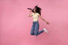 Beautiful Young Woman With Microphone Singing And Jumping On Pink Background