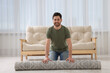 © New Africa - Smiling man unrolling carpet with beautiful pattern on floor in room