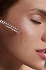 Poster - Beautiful young woman applying cosmetic serum onto her face, closeup