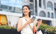 © dodotone - Elegant asian woman using electronic mobile banking app and credit card at outdoors