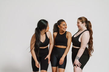 Wall Mural - Group of smiling women in sportswear posing isolated over white wall