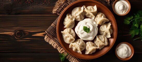 Poster - Traditional Russian pelmeni served in a wooden bowl with butter sour cream and black pepper on isolated pastel background Copy space in a top view