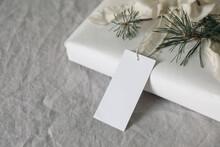 Christmas Present. Empty Gift Tag, Label Mockup. Handmade Gift Wrapping With Cotton Paper, Pine Tree Branches And Silk Ribbon On Linen Table Cloth.Winter Holiday Sale Concept. Blurred Background, Top.