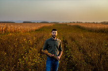 Portrait Of Young Farmer Standing In A Soy Field At Sunset Looking At Camera..
