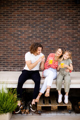 Wall Mural - Family with a mother, father and daughter sitting outside on the steps of a front porch of a brick house