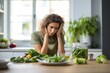 © gankevstock - Woman with a plate of green salad on table in kitchen is depressed during dieting. The concept of negative consequences of a strict diet