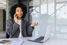 Successful Businesswoman Talking On The Phone Inside The Office At Workplace, African American Woman Smiling Happy Working Using Laptop At Work.
