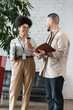 © LIGHTFIELD STUDIOS - cheerful african american woman holding coffee to go and chatting with asian coworker during break